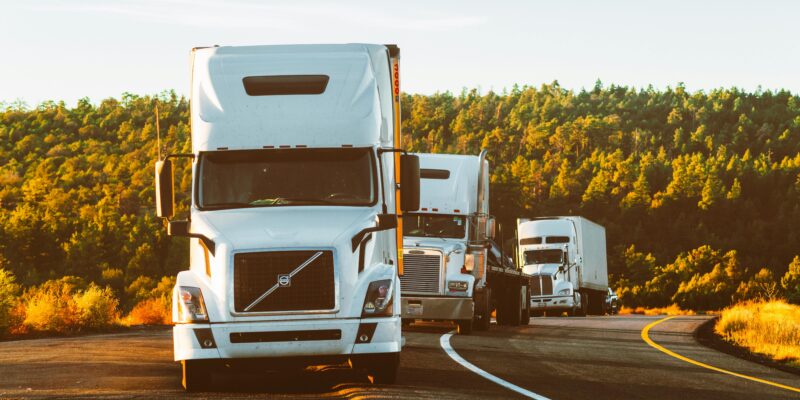 Three semi trucks driving on a highway through a forested landscape in Arizona.