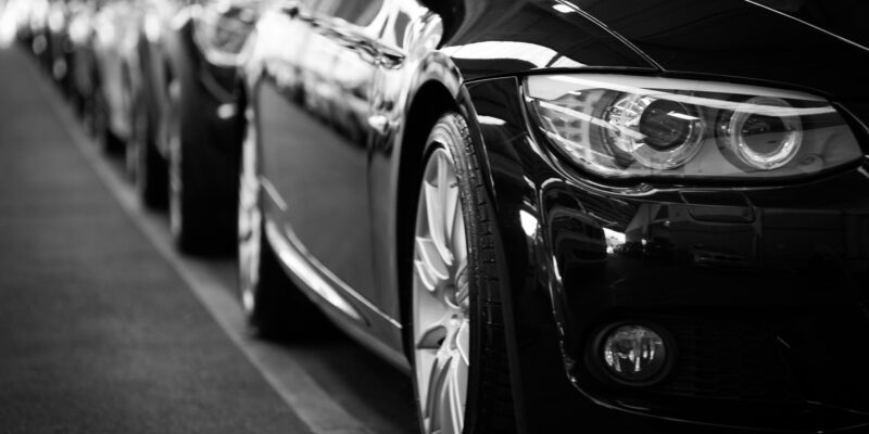 Close-up black and white image of a luxury car line-up focusing on vehicle headlights.