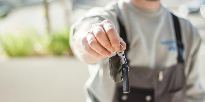 Hand holding a car key outdoors, blurred background, shallow focus.